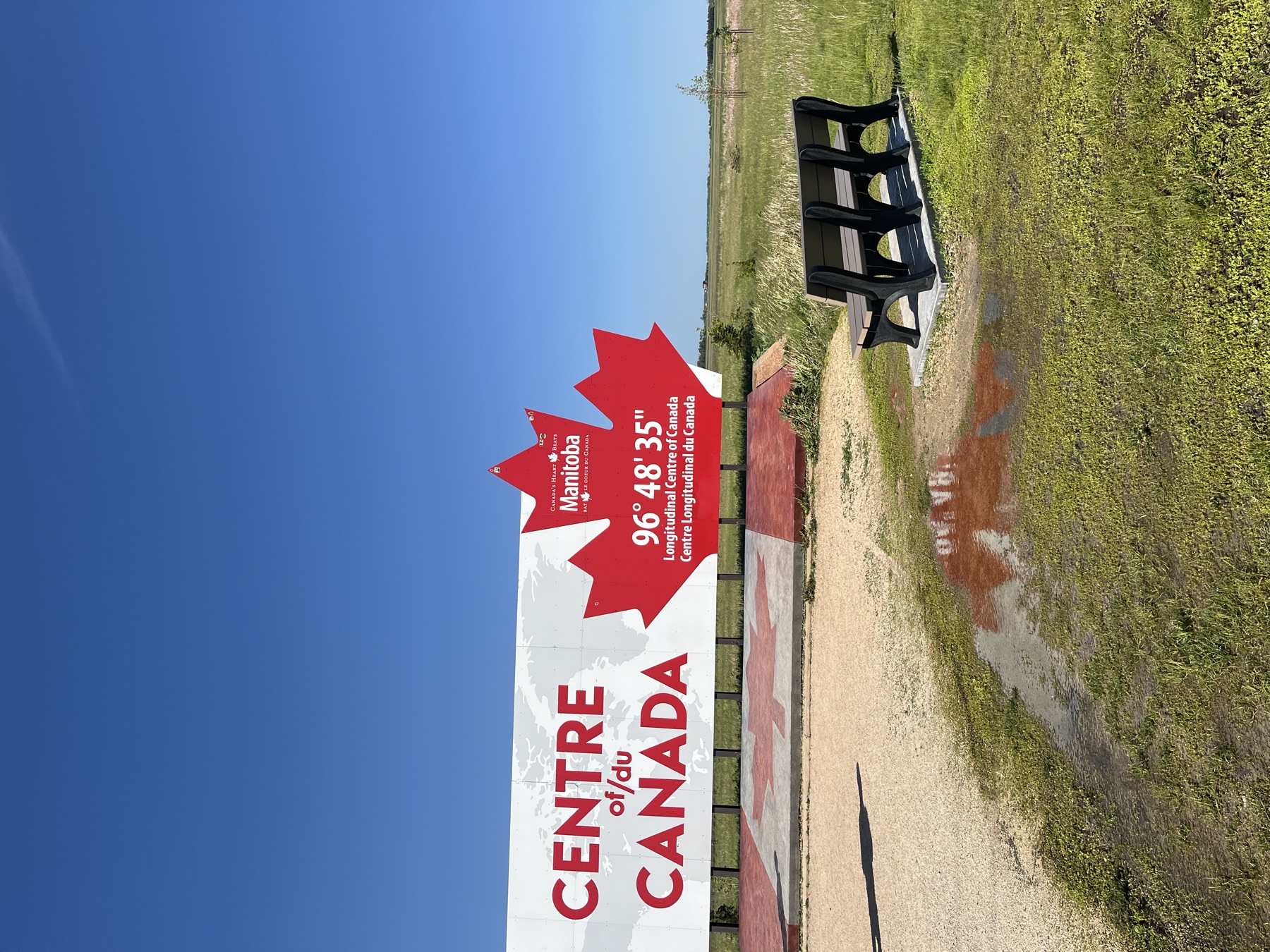 The longitudinal Centre of Canada sign beneath a wide prairie sky